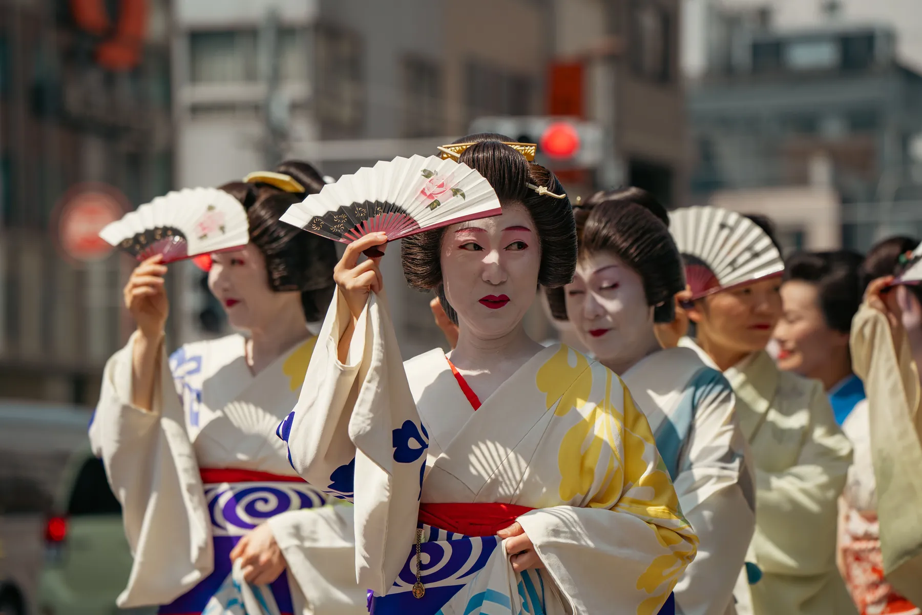 Women in kimono and traditional hairstyles shade their faces with folding fans during a street parade in Tokyo