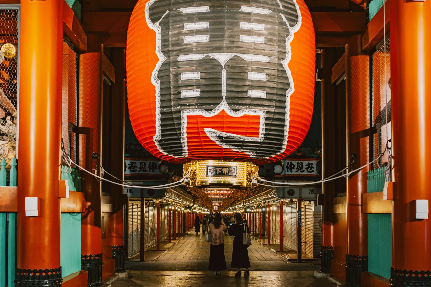 A giant red paper lantern hangs above a lit walkway lined with shops in Asakusa, Tokyo